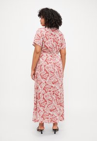 Maxi dress in red with white floral print, short sleeves, back tie detail, and flowing fabric. Textured design features intricate patterns.