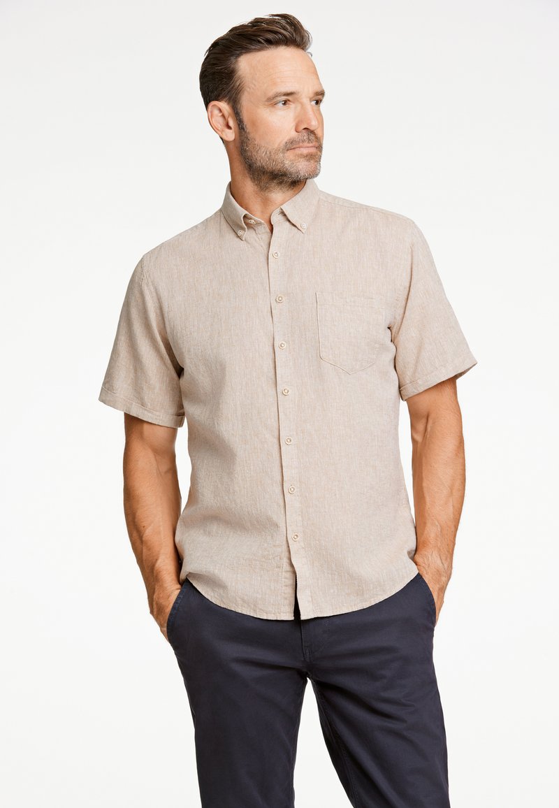 Camisa de botones de manga corta en beige con una textura sutil, bolsillo en el pecho y cuello clásico, combinada con pantalones oscuros.