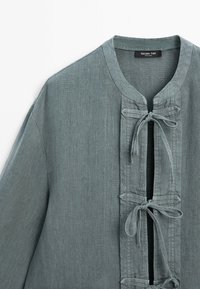 Szaro-zielona lniana koszula z okrągłym kołnierzem i trzema związanymi materiałowymi kokardami z przodu, oznaczona marką Massimo Dutti.