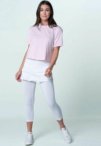 T-shirt corto rosa chiaro, gonna bianca a strati e leggings bianchi. Tessuto morbido, maniche corte e design aderente, abbinati a sneakers bianche.