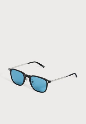 Des lunettes de soleil rectangulaires noires, aux verres bleu vif et aux branches fines argentées, sur un fond clair et uni.