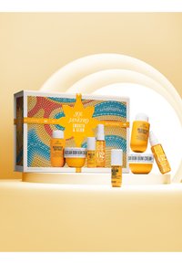 Ensemble de produits de soins de la peau dans des contenants jaunes et blancs variés, présentant une boîte décorative multicolore avec un design d'étoile et du texte.