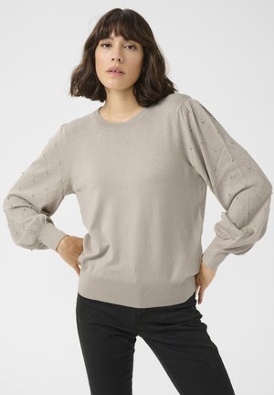 Lichtbeige trui met een ronde halslijn, getextureerde pofmouwen en decoratieve kraalaccenten langs de schouders. Afgerond met een geribbelde zoom.