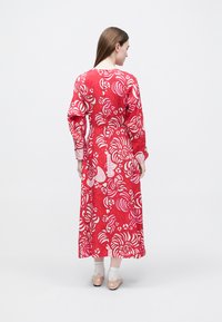 Rotes langärmliges Kleid mit floralem Muster in Rosa und Weiß; verfügt über einen runden Ausschnitt und eine fließende Silhouette. Kombiniert mit hellen Schuhen.