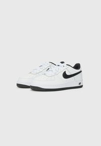 Sapatilhas brancas em couro com detalhes pretos, bico perfurado, design de atacadores e logotipo swoosh em destaque. Sola de borracha preta, estilo minimalista.