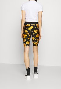 Black bike shorts with a gold baroque pattern, paired with a fitted white crop top and black ankle boots with white soles.