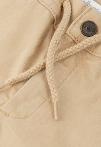 Bermudas de algodón color beige con un cordón trenzado y un detalle de botón de bronce. Textura suave con un patrón de color sólido sutil.