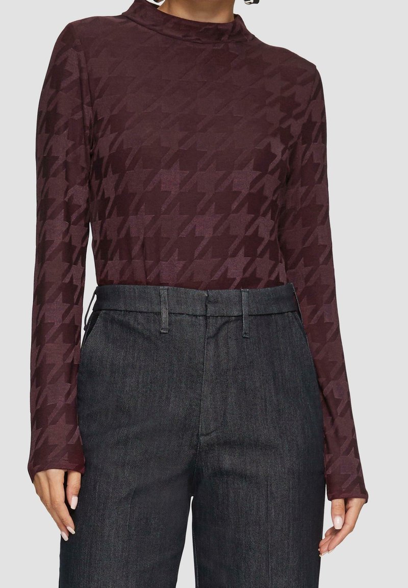 Top burdeos de manga larga con patrón de jaquard, combinado con pantalones de mezclilla oscuros de cintura alta. Textura suave, diseño ajustado y un ligero brillo.