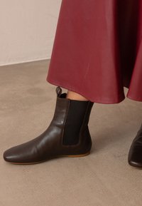 Brązowe skórzane botki za kostkę z elastycznymi bocznymi panelami i tylnym uchwytem, z okrągłym noskiem i cienką gumową podeszwą na teksturowanej powierzchni.