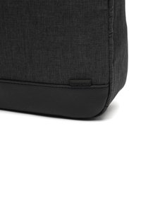 Sivkasta torba z teksturirano površino in črnim usnjenim dnom, z majhno črno oznako. Robovi so rahlo zaobljeni.