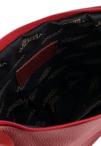 Czerwona skórzana torba o fakturowanym wykończeniu i czarnym wnętrzu z tkaniny. Posiada zamek błyskawiczny oraz wzorzystą podszewkę z brandingiem „Venezia”.