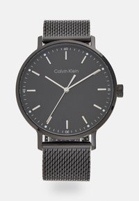 Calvin Klein klokke med svart mesh-reim, rund svart urskive, sølvfargete visere og timemarkører. Minimalistisk design med klare, moderne estetikk.
