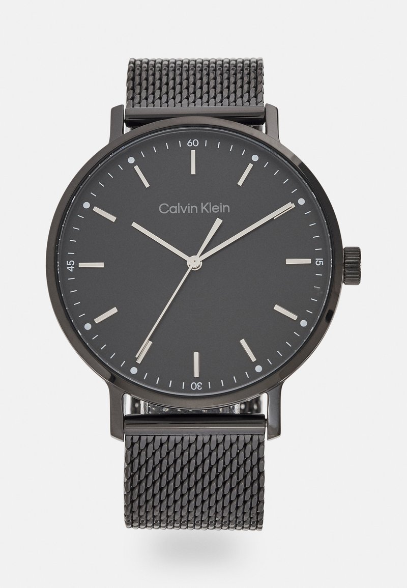 Calvin Klein klokke med svart mesh-reim, rund svart urskive, sølvfargete visere og timemarkører. Minimalistisk design med klare, moderne estetikk.