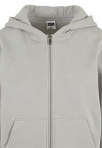 Lys grå hettejakke med glidelås laget av mykt stoff, med foret hette, frontlommer og en solid glidelås. Rent og minimalistisk design.