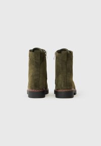 Botas de tobillo de ante verde con un acabado suave, cierre de cremallera lateral y una suela de color marrón con costuras en contraste. Forma robusta, textura mate.