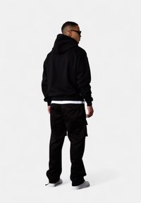 Un sweat à capuche noir et un pantalon cargo noir ample. La tenue présente une texture lisse, avec un sweat doté d'une capuche spacieuse.