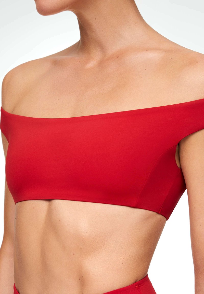 Top court bandeau rouge avec une texture lisse et extensible, design décolleté, et détail découpé sous les bras.