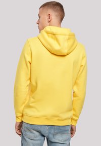 Yellow hoodie with a drawstring hood, soft fabric, ribbed cuffs, and hem. Worn with light blue jeans, showcasing a relaxed fit.