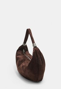 Sac hobo en daim brun avec une forme courbée, accents en métal argenté et fermeture éclair d'un côté. Texture lisse.