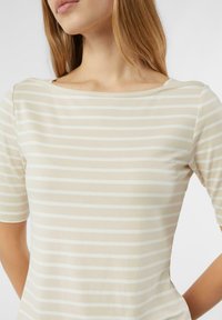 Krótki top z krótkim rękawem w paski z dekoltem w łódkę; wykonany z miękkiej beżowej tkaniny z białymi paskami, zapewnia gładką i lekką fakturę.