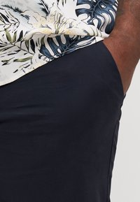 Camisa de manga corta con un patrón floral en azul, blanco y amarillo, combinada con pantalones cortos oscuros de color marino. Textura suave con un corte relajado.