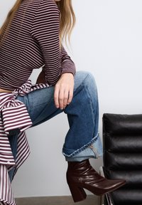 Haut rayé bordeaux à manches longues avec un détail en nœud, associé à un jean en denim bleu clair, ample, et des bottines à talons bordeaux.