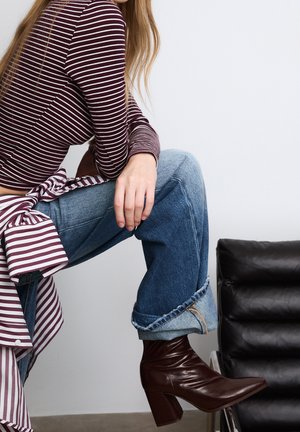 Paskowany bordowy longsleeve z detalem w postaci węzła, zestawiony z jasnoniebieskimi, luźno dopasowanymi dżinsami oraz burgundowymi botkami na obcasie sięgającymi kostki.
