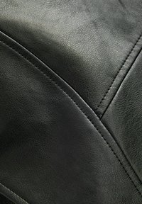 Detailní záběr černé kožené tkaniny s viditelnou strukturou zrnitosti a křížícími se švy, které tvoří geometrické tvary.