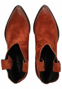 Stivaletti in suede marrone con punta affusolata, dettagli laterali elastici e tacco nero basso. L'interno presenta il logo del marchio in lettere dorate.