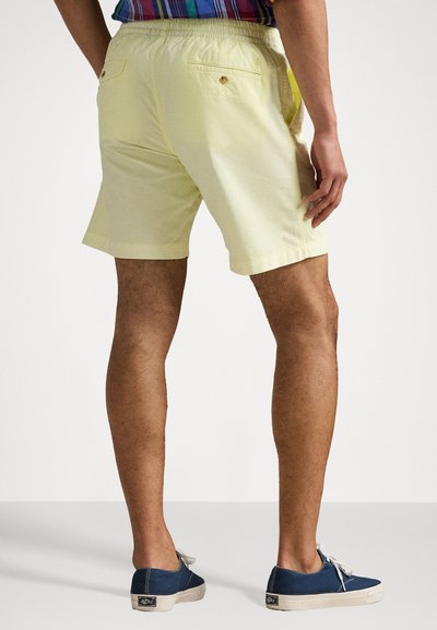 Shorts jaune clair avec une taille élastique, poche arrière avec un bouton et ourlet plat. Associés à des chaussures en toile bleu foncé.