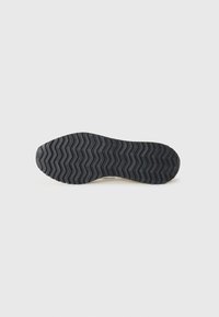 Semelle de chaussure en caoutchouc noir avec un motif de bande de roulement en zigzag et une surface texturée. Les bords sont arrondis ; design épuré sans aucune marque visible ni embellissements.