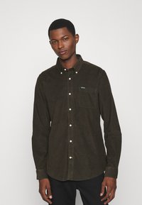 Bruine corduroy button-up shirt met een puntige kraag, borstzak en witte knopen. Heeft een klein groen logo op de zak.