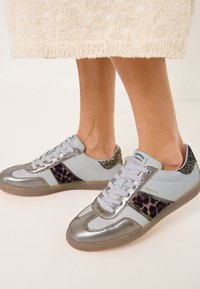 Jasnoniebieskie trampki z metalicznymi srebrnymi akcentami, czarnymi panelami w panterkę i błyszczącym detalem na pięcie. Wiązane, z gumową podeszwą.