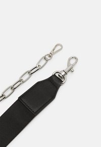 Sangle de sac en tissu noir avec une extrémité en cuir noir texturé et des moustaches en métal argenté, accompagnée d'une chaîne en métal argenté avec un fermoir assorti.