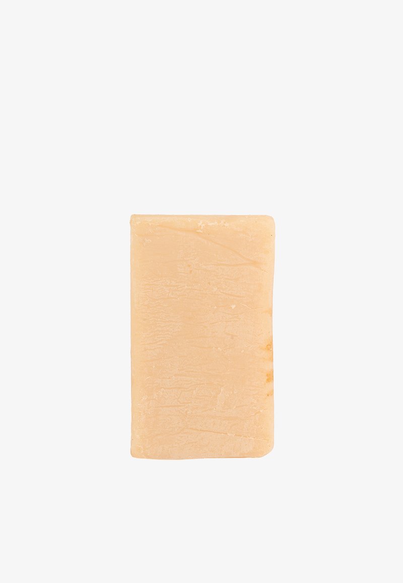 Barra di sapone rettangolare beige con una superficie leggermente texture, fotografata su uno sfondo bianco.