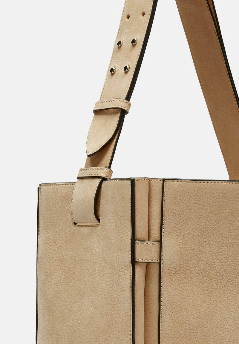Beige Lederhandtasche mit strukturierter Oberfläche, ausgestattet mit einem abnehmbaren Trageriemen, kontrastierenden schwarzen Kanten und silberfarbenen Hardware-Elementen.