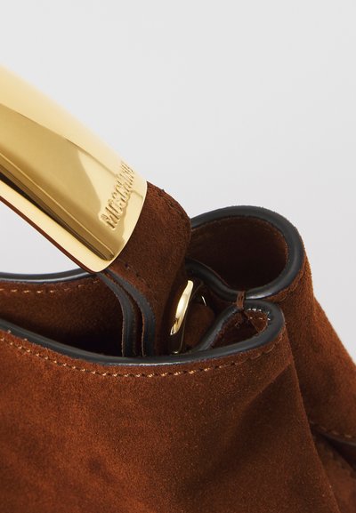 Brown suede handbag with black trim and shiny gold handle engraved with brand name, showing close-up detail of texture and stitching.