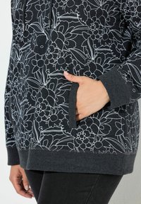 Felpa grigia scura con stampa floreale bianca, tasca frontale e polsini e orlo a costine. Tessuto morbidissimo con vestibilità rilassata.