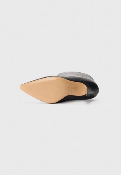 Botte de cheville en cuir noir avec un bout pointu et une semelle marron. Présente une texture lisse avec un design élégant et des accents minimalistes.