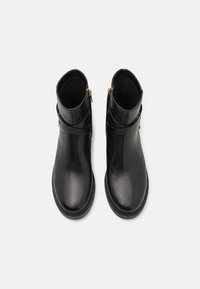 Bottes noires en cuir à la cheville avec une finition lisse, présentant une fermeture éclair sur le côté et une semelle en caoutchouc texturé. Design étroit avec des accents minimalistes.