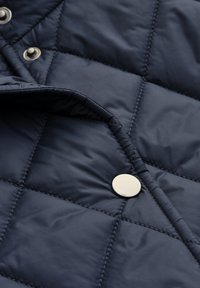 Marineblau gesteppte Jacke mit glänzendem silbernen Druckknopf, glatter Textur und Nähten im Rautenmuster. Verstellbarer Kragen.