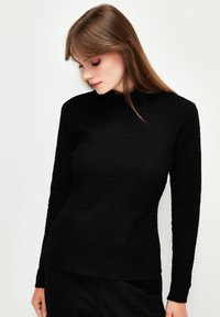 Schwarzes Longsleeve-Oberteil aus strukturiertem Stoff mit hohem Kragen. Es hat eine figurbetonte Form und eine glatte Silhouette, die sich gut zum Überziehen eignet.