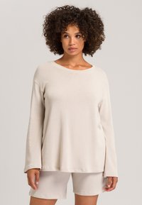 Beige pitkähihaine paita pyöreällä kaula-aukolla ja laskeutuvilla harteilla, yhdistettynä vastaaviin shortseihin. Pehmeä, kevytrakenteinen kangas rentoa istuvuutta varten.