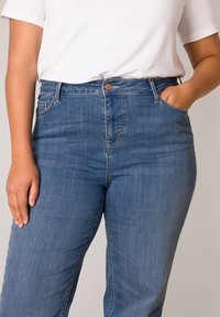 Blauwe denim jeans met een hoge taille, zijzakken en een bronzen knoopsluiting. Glad textuur met subtiele vervaging langs de benen.