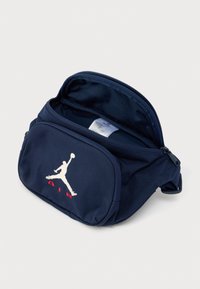 Τσάντα από ύφασμα σε ναυτικό μπλε με φερμουάρ μπροστά, που διαθέτει το εμβληματικό λευκό λογότυπο Jumpman και κόκκινο κείμενο "AIR". Λεία υφή και συμπαγής σχεδίαση.