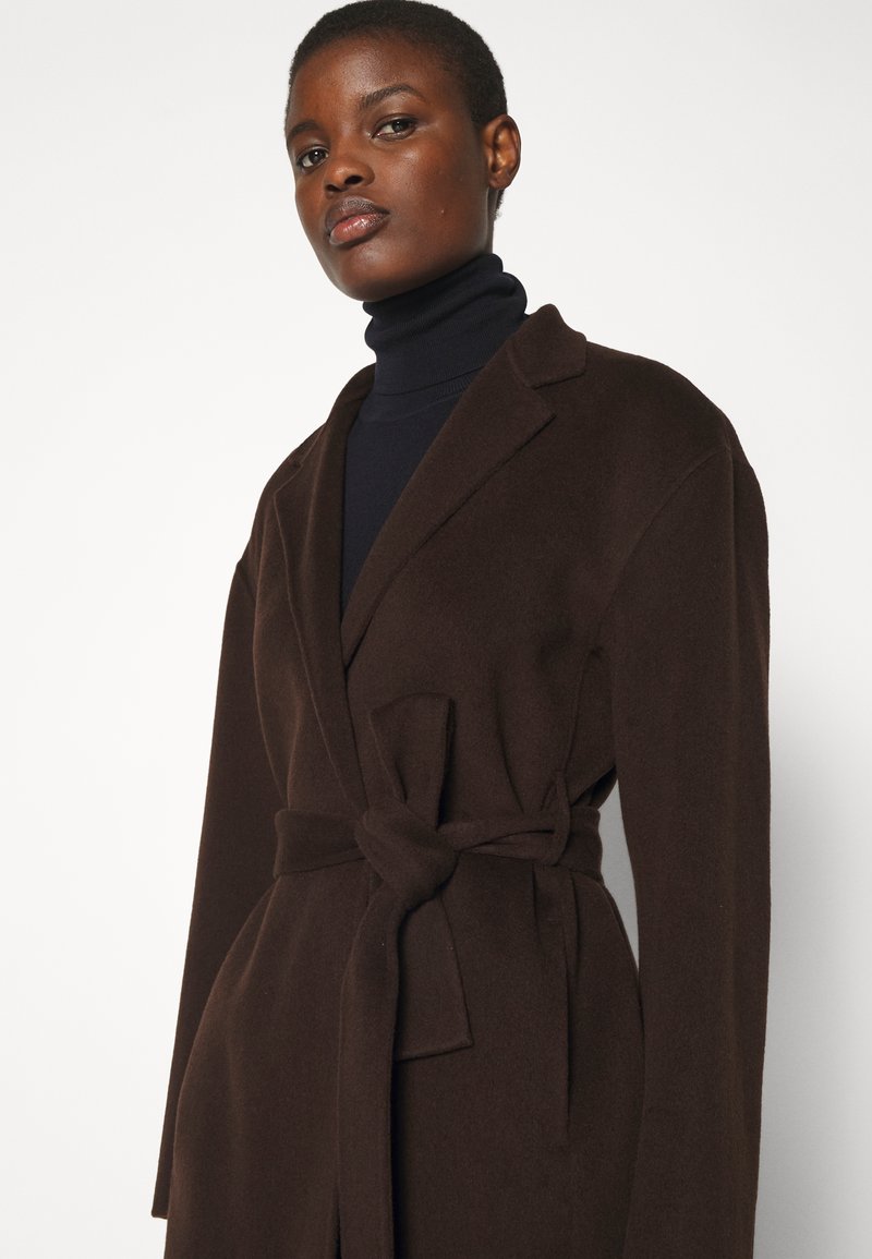 Brun bæltejakke lavet af blødt stof med krave, lange ærmer og en knyttet sløjfe i taljen, der viser en glat tekstur.