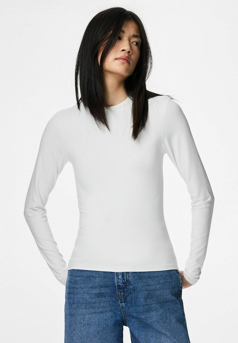 Maglia bianca a maniche lunghe con scollo rotondo e texture liscia, abbinata a jeans di denim blu. Design semplice, senza motivi o dettagli.