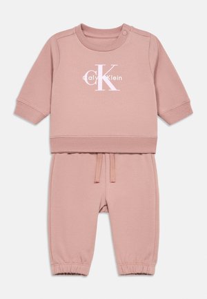 Vaaleanpunainen Calvin Klein -vauvan pitkähihainen asu, jossa on joustavat hihansuut, nyörillä kiristettävät housut ja rintamuksessa logo.