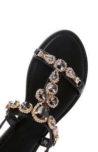 Sandalo nero con design a T decorato con cristalli, dettagli dorati e superficie in pelle liscia. Incluso cinturino ankle regolabile.