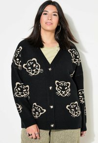 Mustapaita, jossa on V-pääntie ja beige leopardikuvio. Siinä on suuret napit ja pudotetut olkapäät rentoa istuvuutta varten.